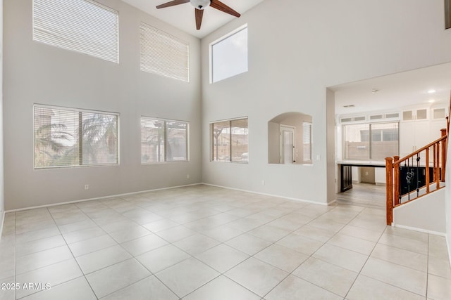 unfurnished living room featuring a ceiling fan, stairway, arched walkways, light tile patterned floors, and baseboards