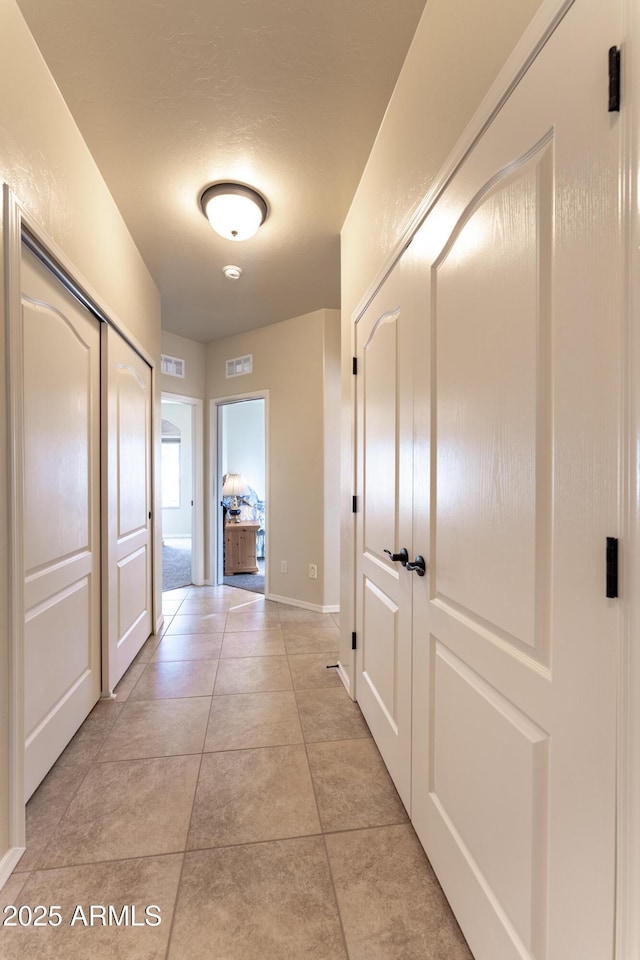 hall featuring light tile patterned flooring, baseboards, and visible vents