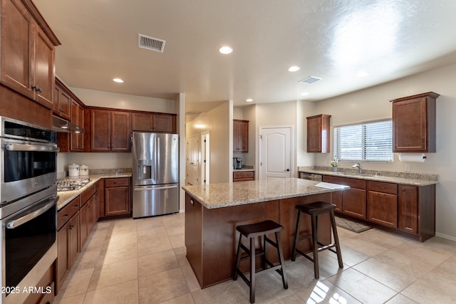 kitchen with visible vents, stainless steel appliances, under cabinet range hood, a sink, and a center island