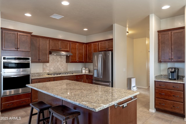 kitchen featuring stainless steel appliances, a center island, tasteful backsplash, under cabinet range hood, and a kitchen breakfast bar