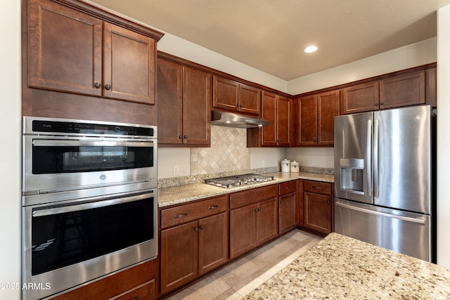 kitchen with light stone countertops, recessed lighting, tasteful backsplash, appliances with stainless steel finishes, and under cabinet range hood
