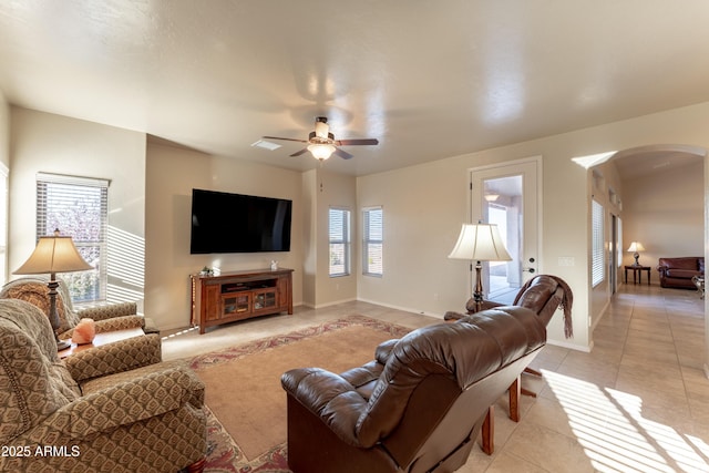 living area featuring arched walkways, a ceiling fan, baseboards, and light tile patterned flooring