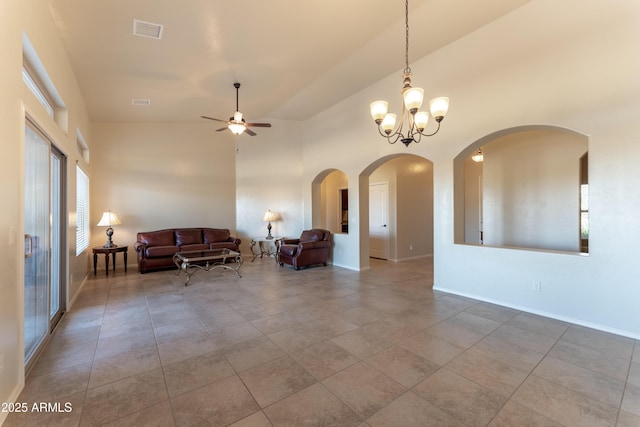 unfurnished living room with ceiling fan with notable chandelier, baseboards, a high ceiling, arched walkways, and visible vents