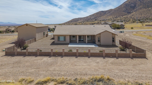 rear view of house featuring a patio, a mountain view, stucco siding, and a fenced front yard