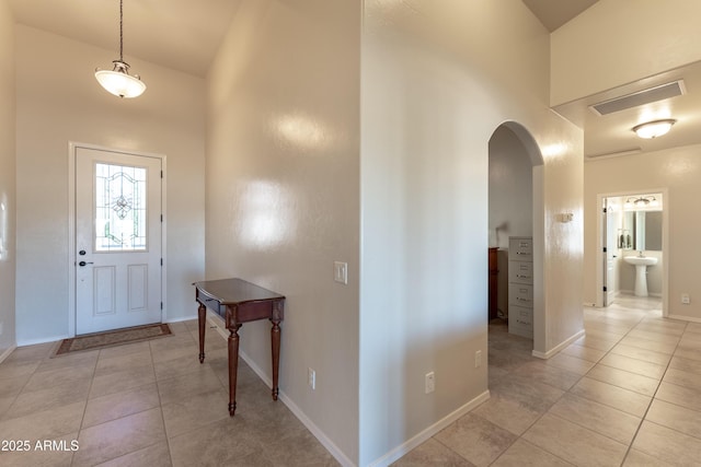 foyer featuring arched walkways, a high ceiling, baseboards, and light tile patterned floors
