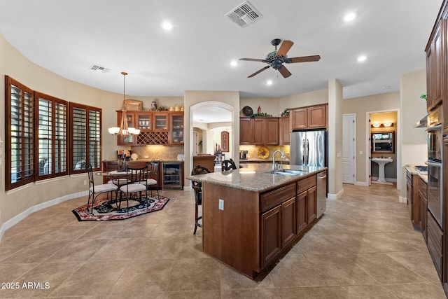 kitchen featuring sink, tasteful backsplash, light stone counters, a kitchen bar, and a kitchen island with sink