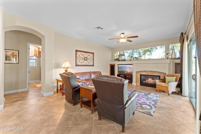 living room with a tiled fireplace, ceiling fan, light tile patterned flooring, and a healthy amount of sunlight