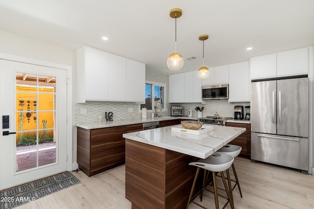 kitchen with backsplash, a kitchen bar, appliances with stainless steel finishes, and light wood-style flooring