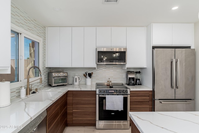 kitchen featuring modern cabinets, a sink, stainless steel appliances, light stone counters, and backsplash