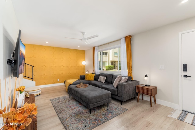 living room with light wood finished floors, a ceiling fan, an accent wall, and baseboards