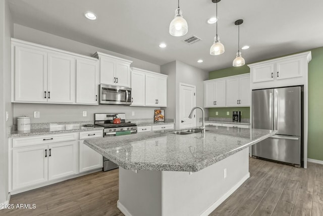 kitchen featuring hanging light fixtures, wood finished floors, a sink, stainless steel appliances, and white cabinets