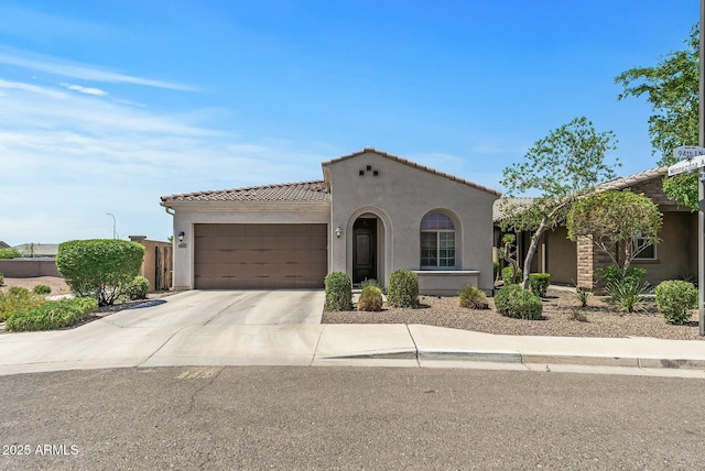 mediterranean / spanish-style house featuring an attached garage, a tiled roof, stucco siding, and concrete driveway