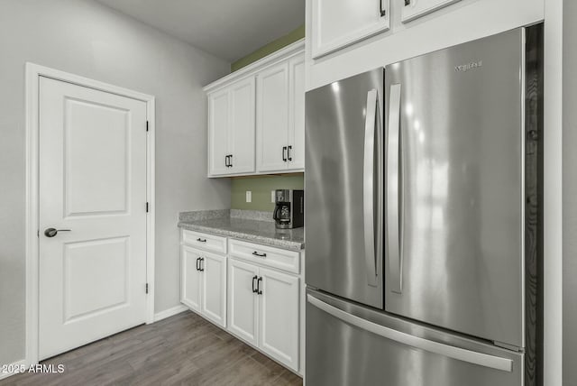 kitchen featuring freestanding refrigerator, wood finished floors, light stone countertops, and white cabinetry