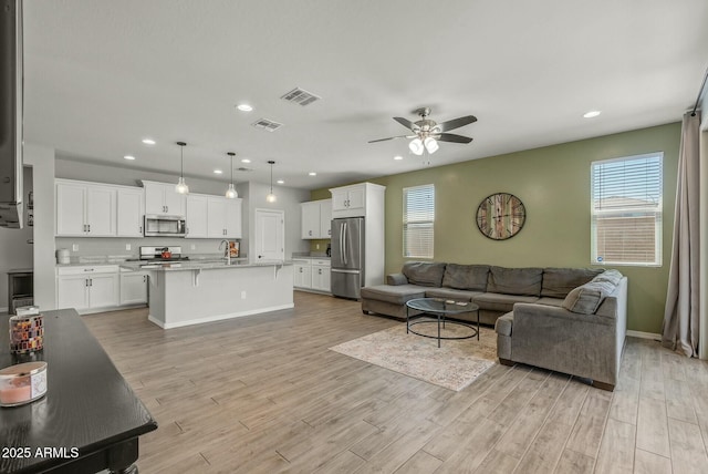 living area with light wood-style flooring, visible vents, and ceiling fan