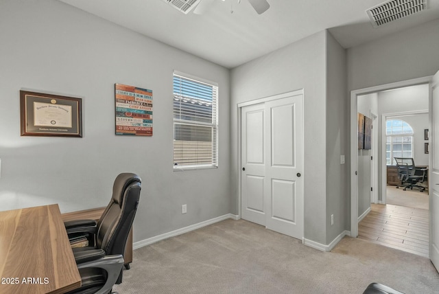 office area with light carpet, a ceiling fan, visible vents, and baseboards
