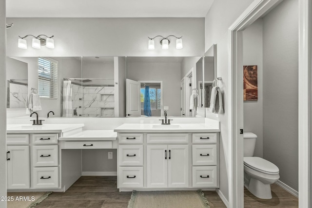 bathroom featuring wood finished floors, toilet, a sink, two vanities, and tiled shower
