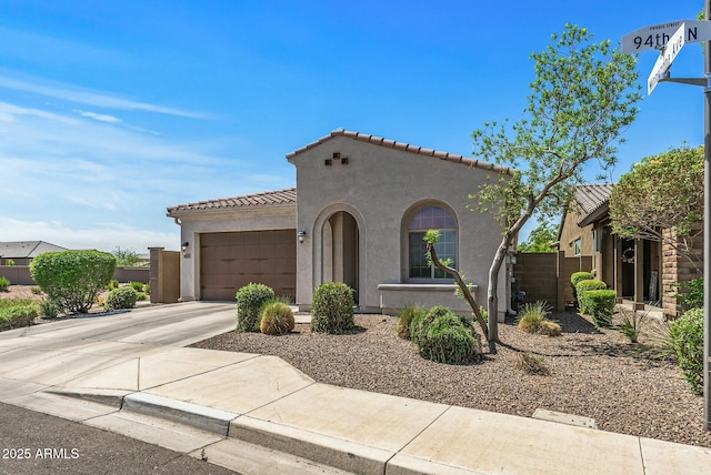 mediterranean / spanish home with concrete driveway, a tiled roof, fence, a garage, and stucco siding