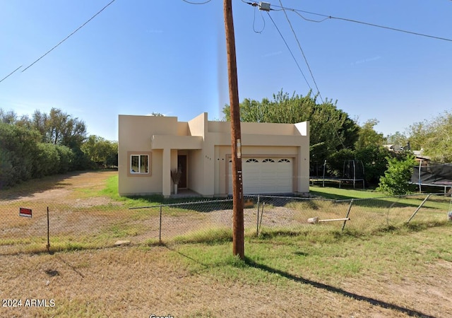 adobe home with a trampoline, a front lawn, and a garage