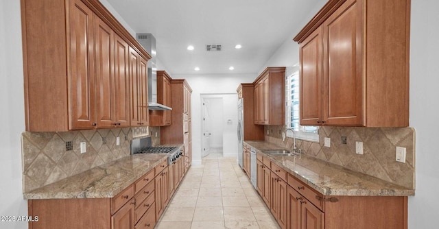 kitchen with sink, wall chimney range hood, appliances with stainless steel finishes, light stone countertops, and decorative backsplash