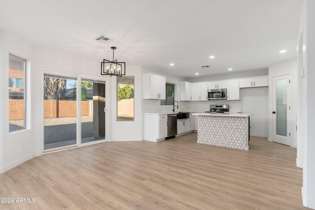 kitchen with hanging light fixtures, a center island, white cabinets, appliances with stainless steel finishes, and light hardwood / wood-style floors