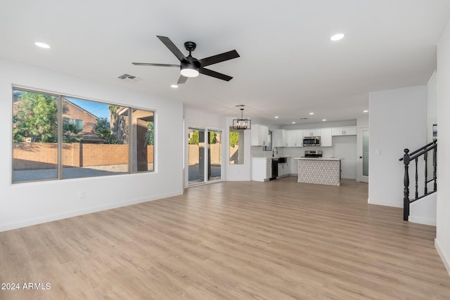 unfurnished living room with light hardwood / wood-style floors, sink, and ceiling fan with notable chandelier