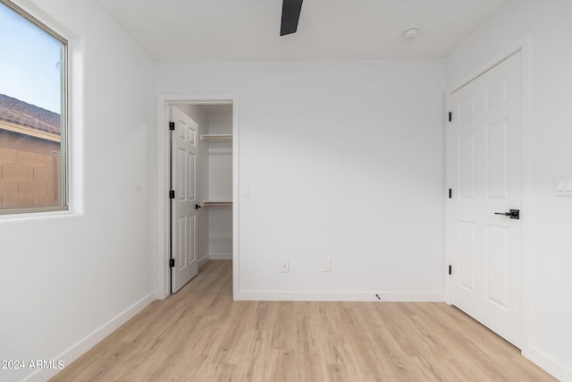 unfurnished bedroom featuring light hardwood / wood-style floors, a walk in closet, a closet, and ceiling fan