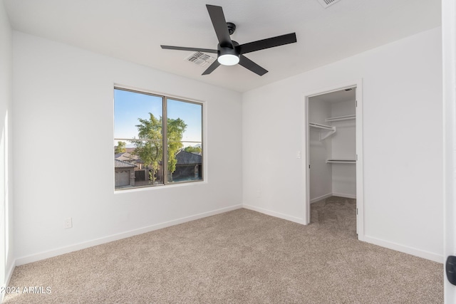 unfurnished bedroom with light carpet, a walk in closet, a closet, and ceiling fan