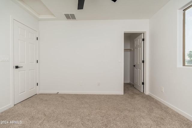 unfurnished bedroom featuring a closet, light carpet, a walk in closet, and ceiling fan