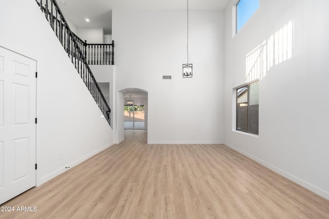 unfurnished living room with light hardwood / wood-style flooring, a towering ceiling, and plenty of natural light