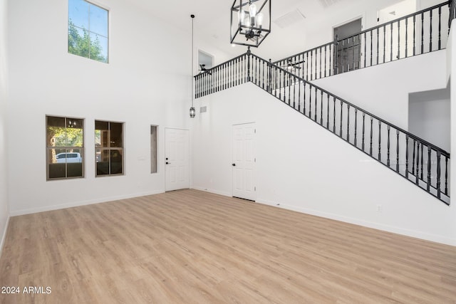 unfurnished living room with an inviting chandelier, a high ceiling, and light hardwood / wood-style floors