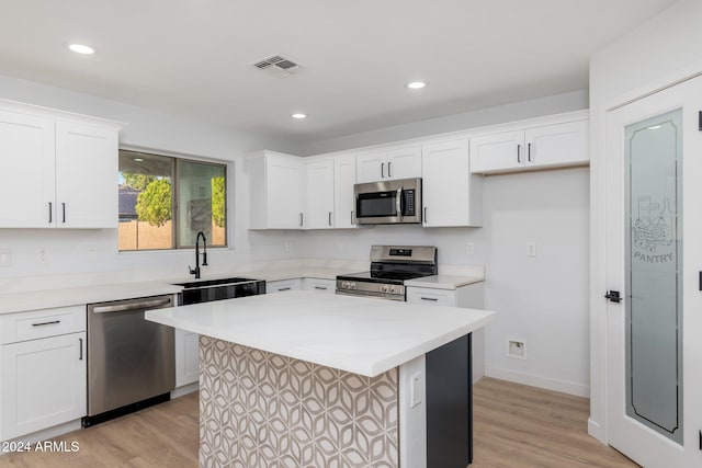 kitchen featuring white cabinets, light hardwood / wood-style flooring, stainless steel appliances, sink, and a center island