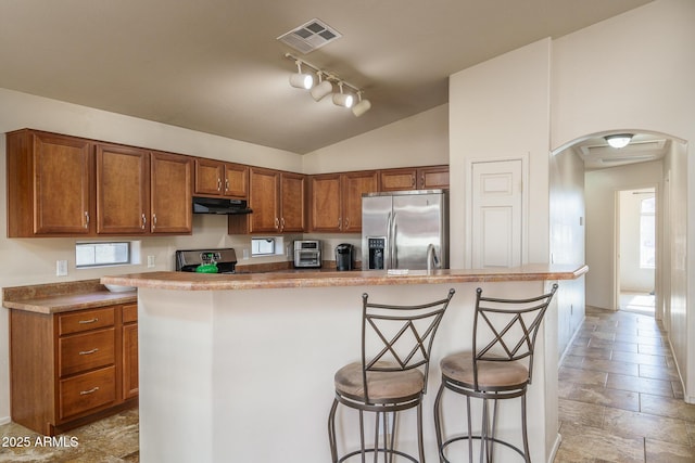 kitchen featuring a kitchen breakfast bar, a kitchen island with sink, stainless steel appliances, track lighting, and lofted ceiling