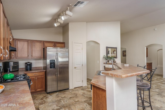 kitchen with a kitchen breakfast bar, a center island with sink, stainless steel fridge with ice dispenser, black gas range oven, and sink