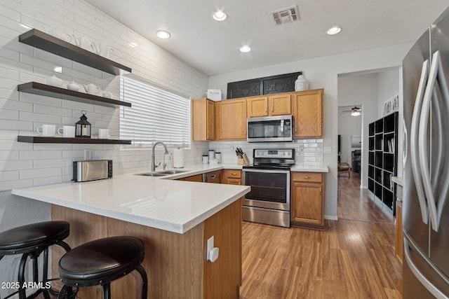 kitchen featuring stainless steel appliances, visible vents, light wood-style floors, a sink, and a peninsula