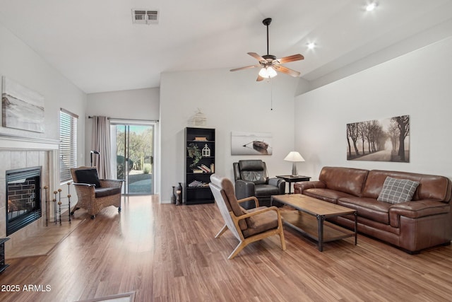 living area featuring high vaulted ceiling, visible vents, a ceiling fan, light wood-type flooring, and a tiled fireplace