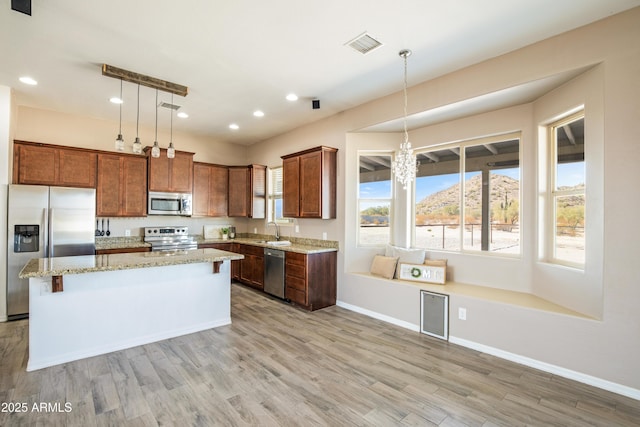 kitchen featuring sink, hanging light fixtures, stainless steel appliances, light hardwood / wood-style floors, and a kitchen island