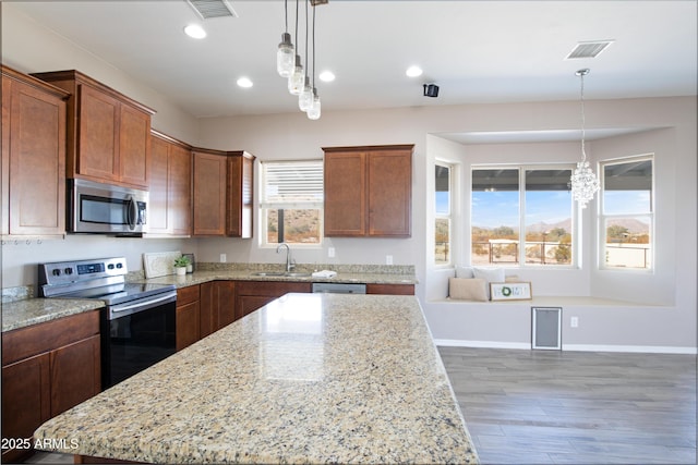 kitchen with a kitchen island, sink, hanging light fixtures, stainless steel appliances, and light stone countertops