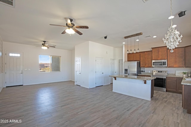 kitchen with a breakfast bar, decorative light fixtures, light wood-type flooring, appliances with stainless steel finishes, and a kitchen island