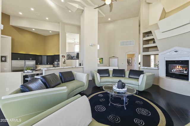 living room with a high ceiling, built in shelves, ceiling fan, a healthy amount of sunlight, and wood-type flooring