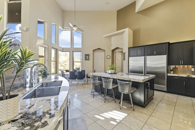 kitchen featuring ceiling fan, decorative backsplash, a towering ceiling, and sink