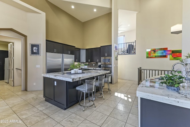 kitchen with light stone countertops, a high ceiling, a kitchen breakfast bar, backsplash, and built in appliances