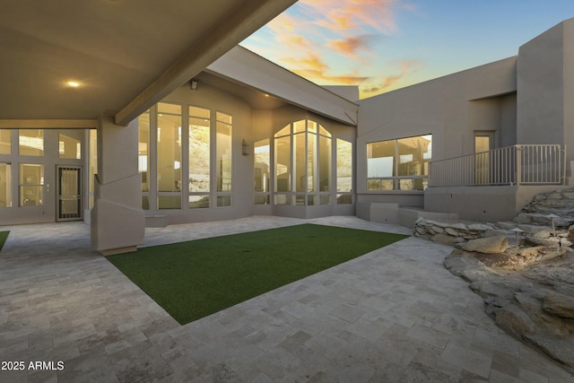 back house at dusk featuring a patio area and a yard