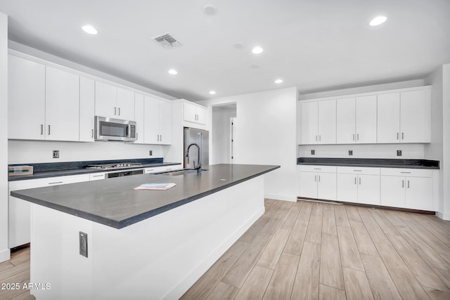 kitchen featuring white cabinetry, a center island with sink, stainless steel appliances, light hardwood / wood-style flooring, and sink