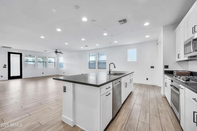 kitchen featuring white cabinetry, stainless steel appliances, sink, ceiling fan, and a center island with sink