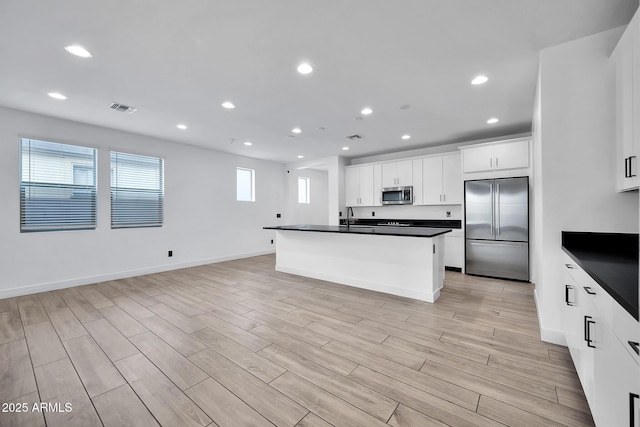 kitchen with appliances with stainless steel finishes, light wood-type flooring, a kitchen island, white cabinets, and sink