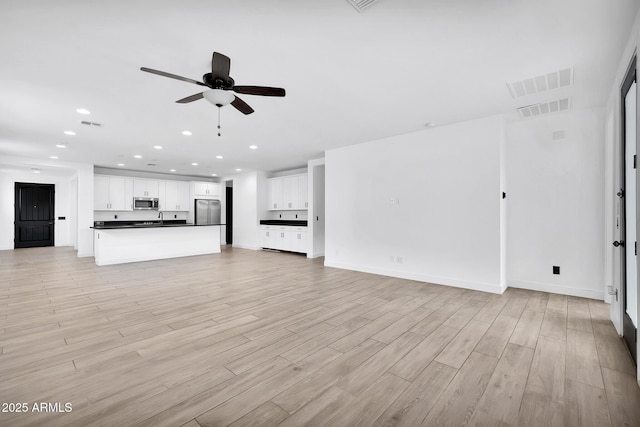 unfurnished living room featuring ceiling fan, sink, and light hardwood / wood-style floors