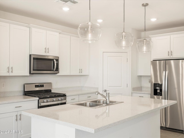 kitchen featuring white cabinets, stainless steel appliances, hanging light fixtures, and an island with sink