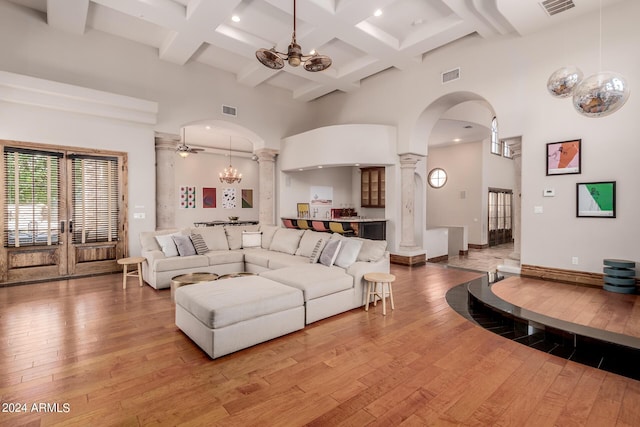 living room featuring a towering ceiling, light hardwood / wood-style floors, decorative columns, and a notable chandelier