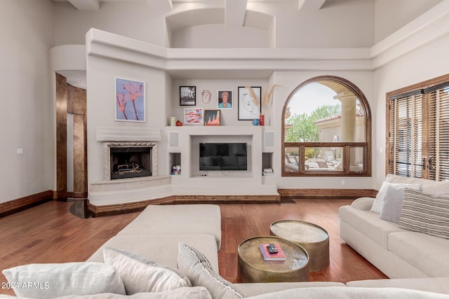 living room with a fireplace, hardwood / wood-style floors, beamed ceiling, and a high ceiling