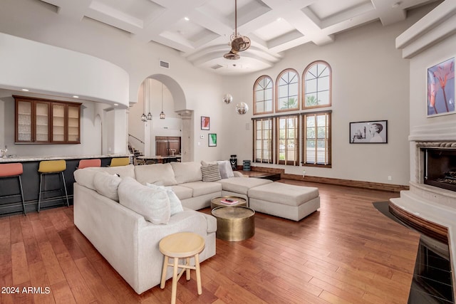 living room with beamed ceiling, wood-type flooring, a towering ceiling, and coffered ceiling